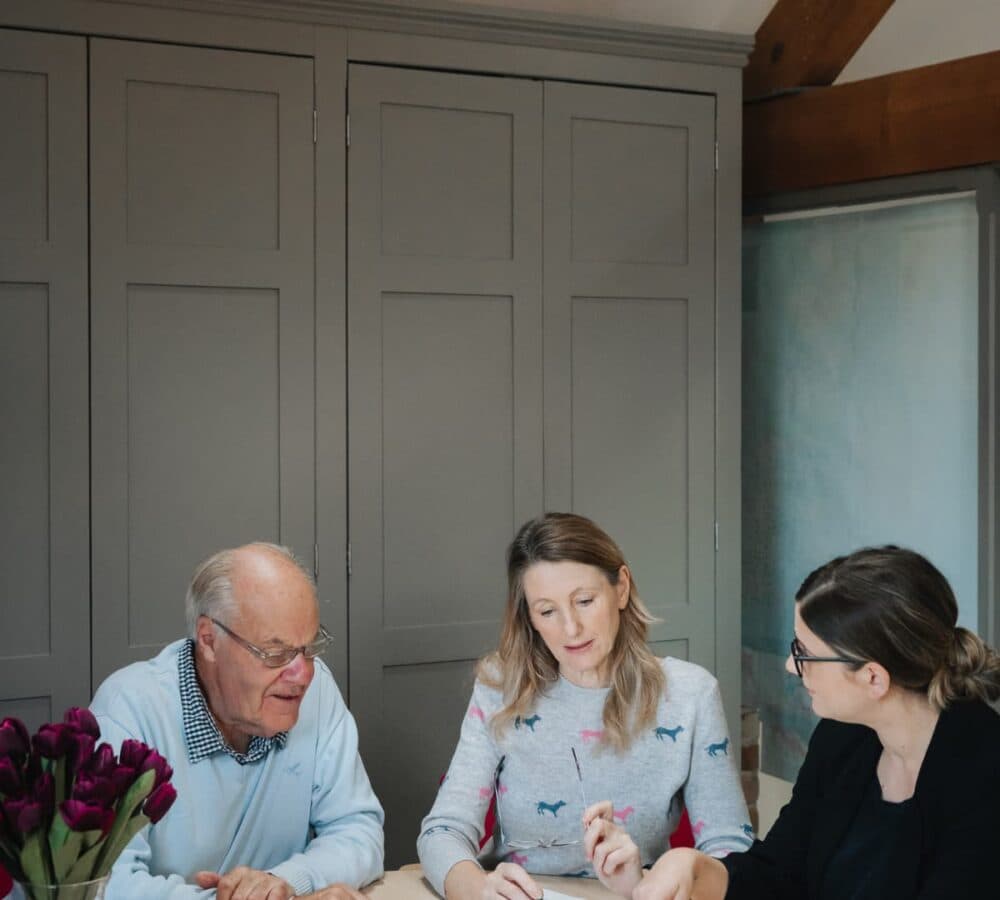 A senior man with his daugher speaking to a care consultant and all are looking at documents while sitting down inside the room