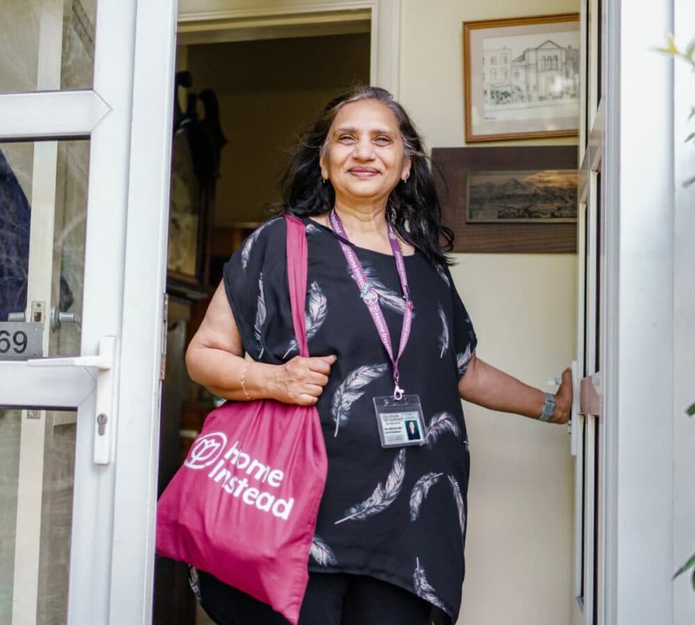 Woman going out of the door with long black hair smiling while carrying a Home Instead bag