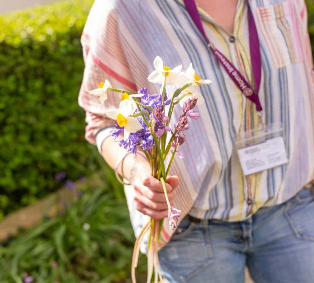 Woman wearing pants and colorful shirts walking while holding colorful flowers