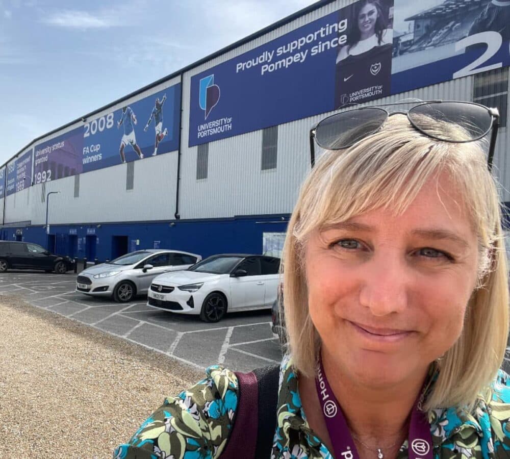 Woman smiling with sunglasses on top of her head and with short hair with cars in the background and a clear sky