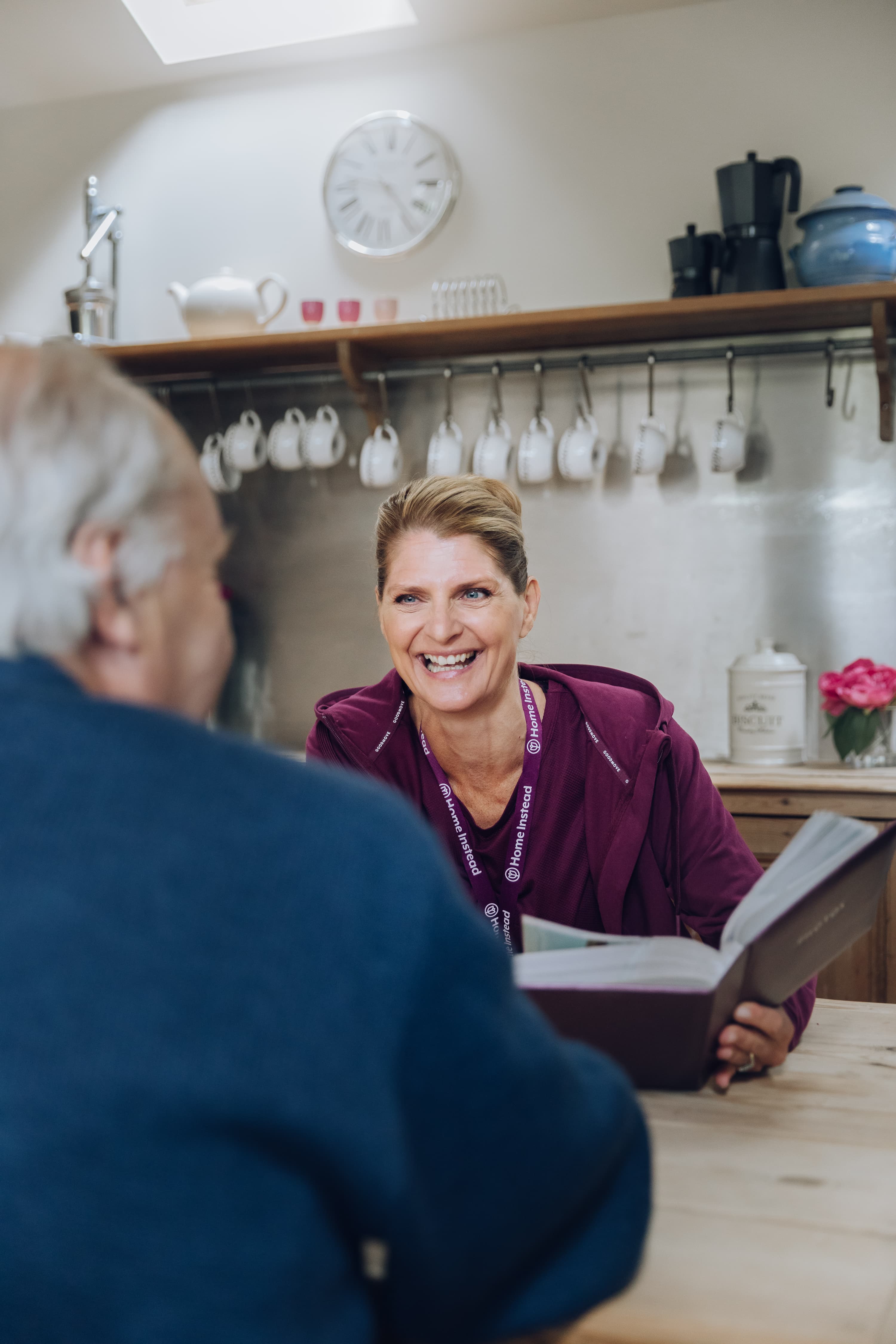 Female Home Instead Care Professional looking at a photo album with a male client during a support in Renfrewshire.