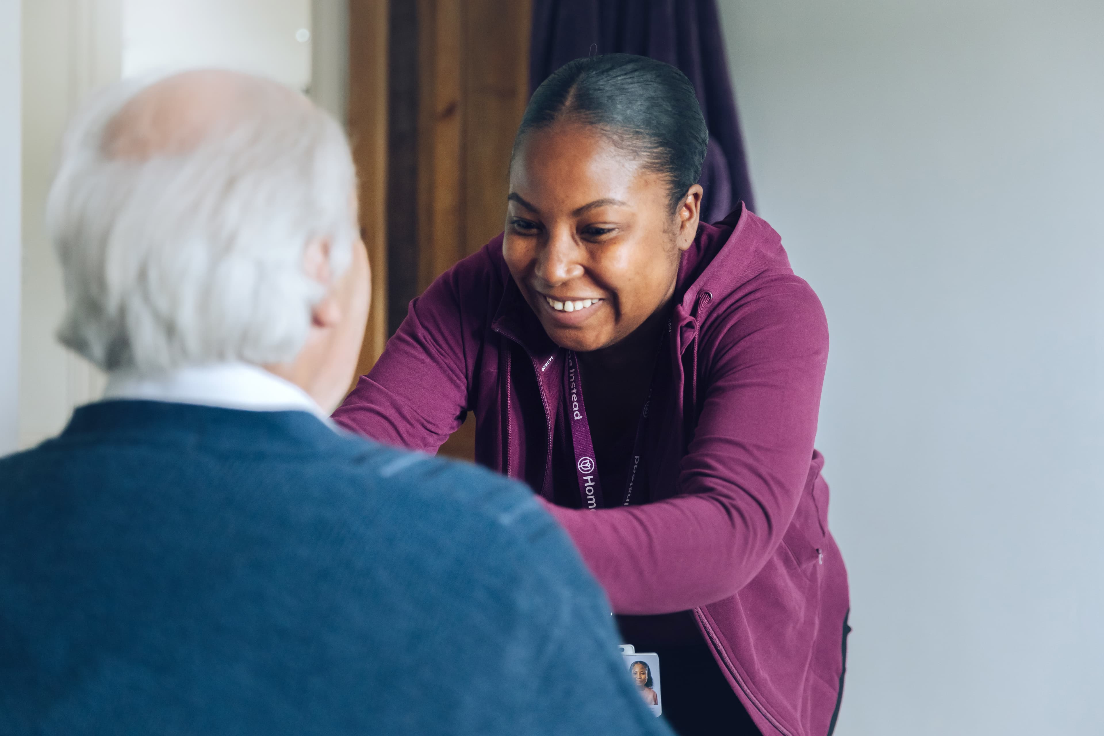 A smiling caregiver helps an older man, reaching out with both arms in a friendly, supportive gesture. - Home Instead
