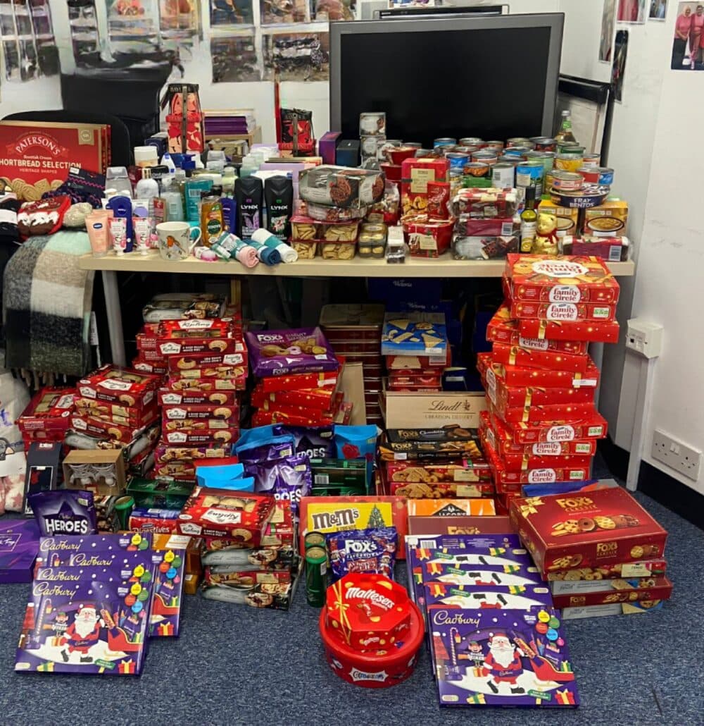 A large assortment of food, snacks, and toiletries stacked on and under a desk in an office space. - Home Instead