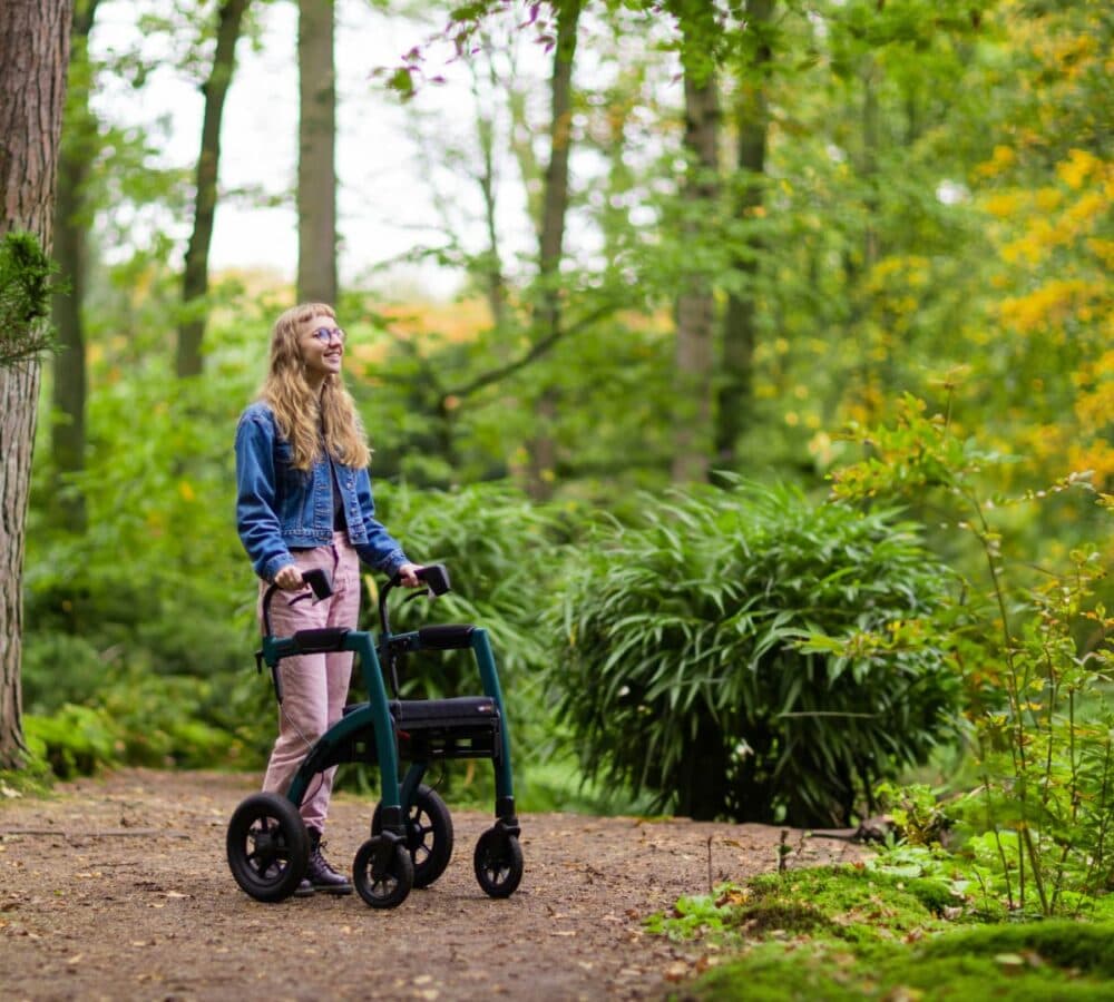 A lady using a walker outdoor smiling and happy and surrounded by lots of plants and tress