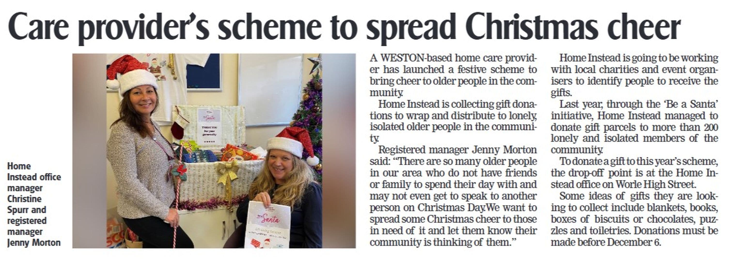Two women in Santa hats stand by a Christmas gift donation box at a care provider's festive event. - Home Instead