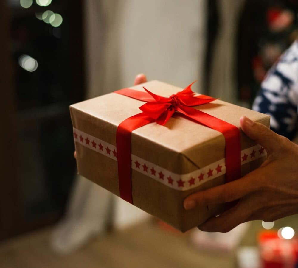 Holding a gift box wrapped in brown with a red ribbon