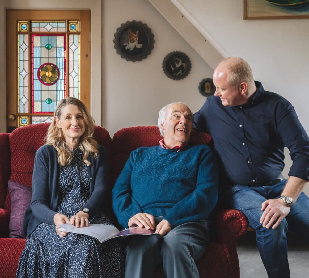 A family sitting together on the couch inside the house, all are happy and smiling