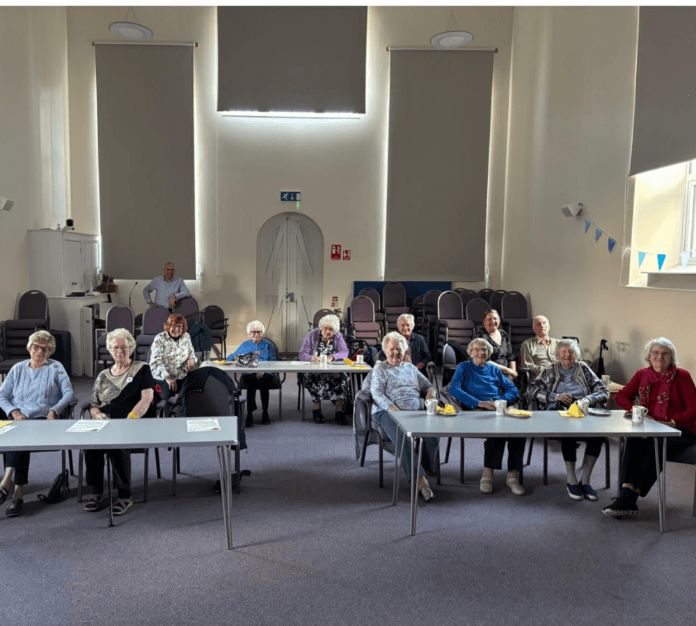 Group of seniors watching a movie happily inside a room with tables and cups and papers on top