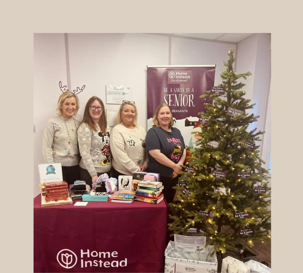 Four women smiling and happy beside a Christmas tree with table and gifts beside them