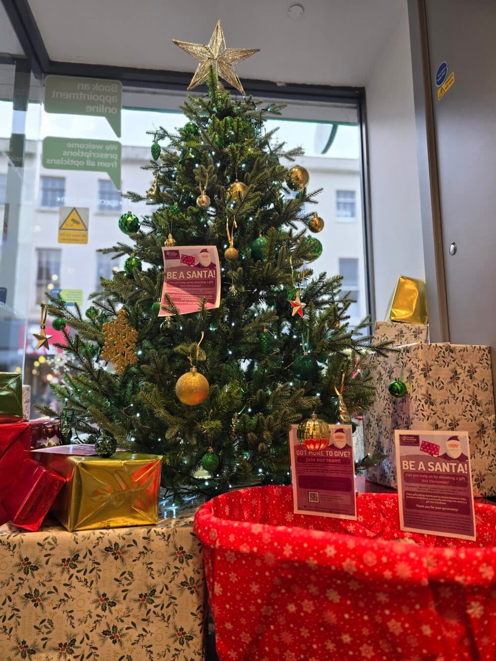 Home Instead Taunton Be A Santa gift collection basket under the Christmas tree at Specsavers Taunton