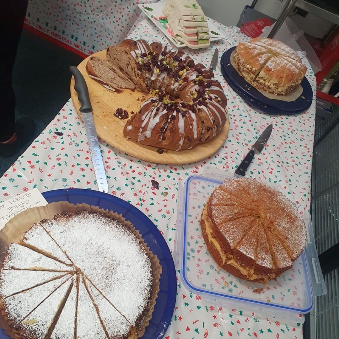 A table with various cakes, a bundt cake, and a plate of sandwiches on a festive tablecloth. - Home Instead