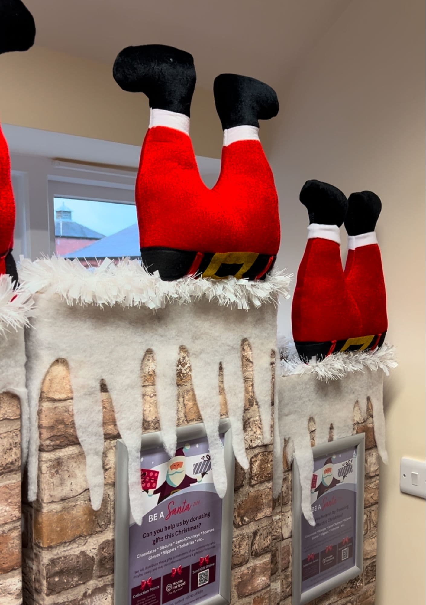 Stuffed Santa legs sticking out of fake chimneys decorated with snow inside a room with cream-colored walls. - Home Instead