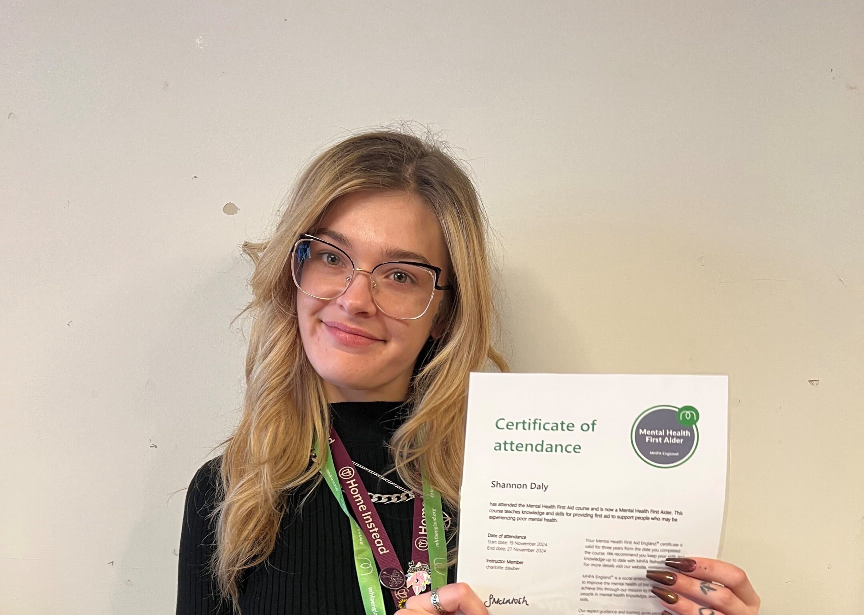 Young woman wearing ID lanyards for Home Instead holding aloft her certificate and smiling