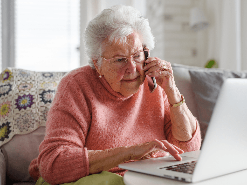 Old lady talking on the phone and looking at laptop