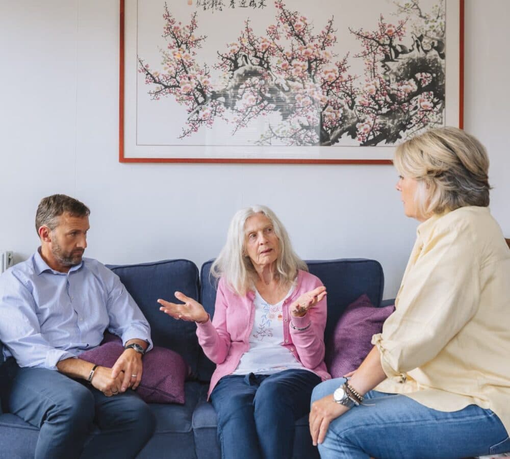 Senior woman with daughter and son talking together while sitting on a blue couch inside the house