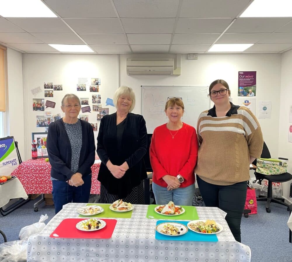Four women inside the office and happy with several plates with food on the table
