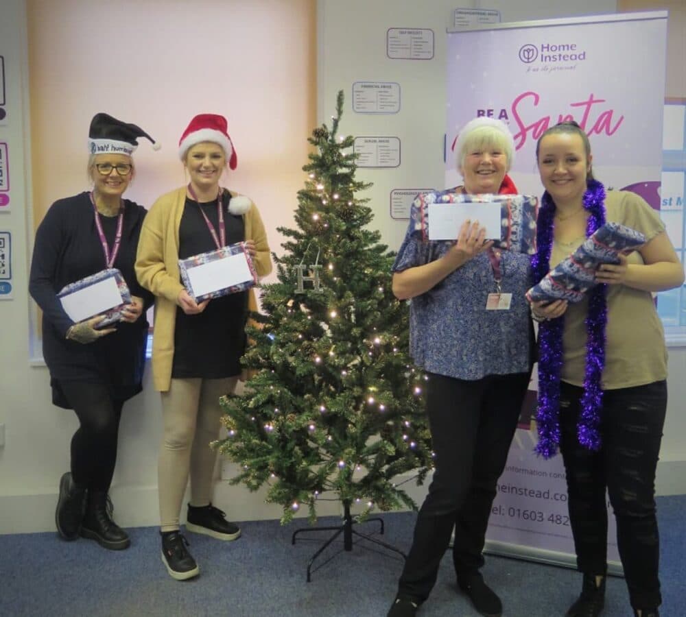 Four ladies wearing santa hat and holding a certificate inside the office with a Christmas tree at the middle
