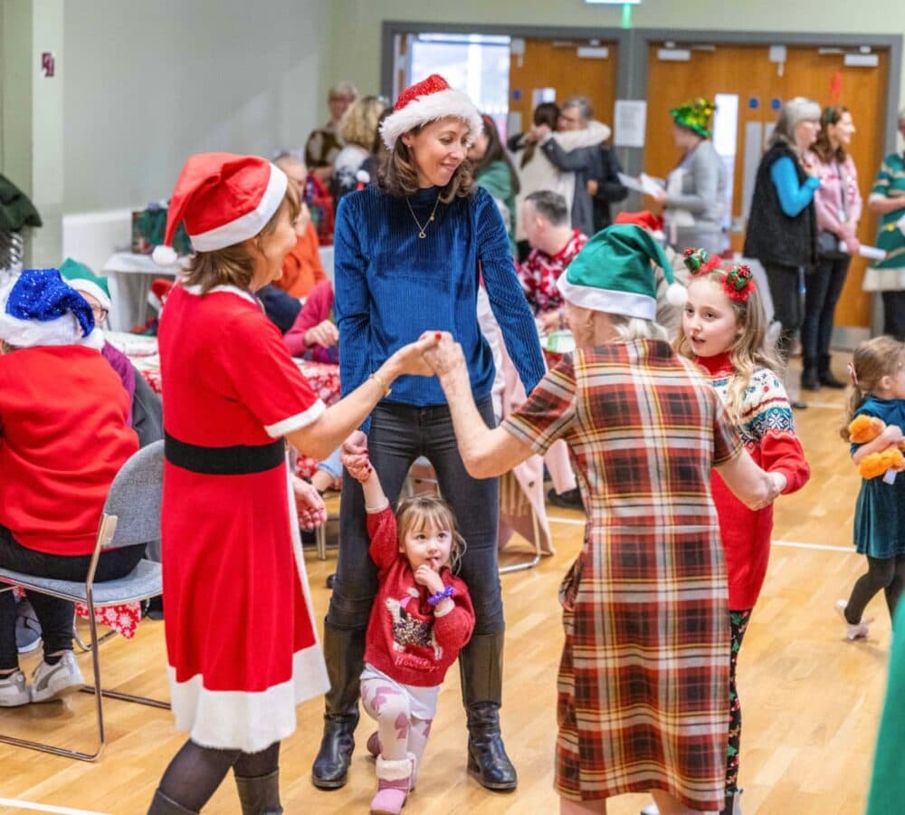 Women and kids happily dancing while some are wearing Santa hat and holding each other's hand