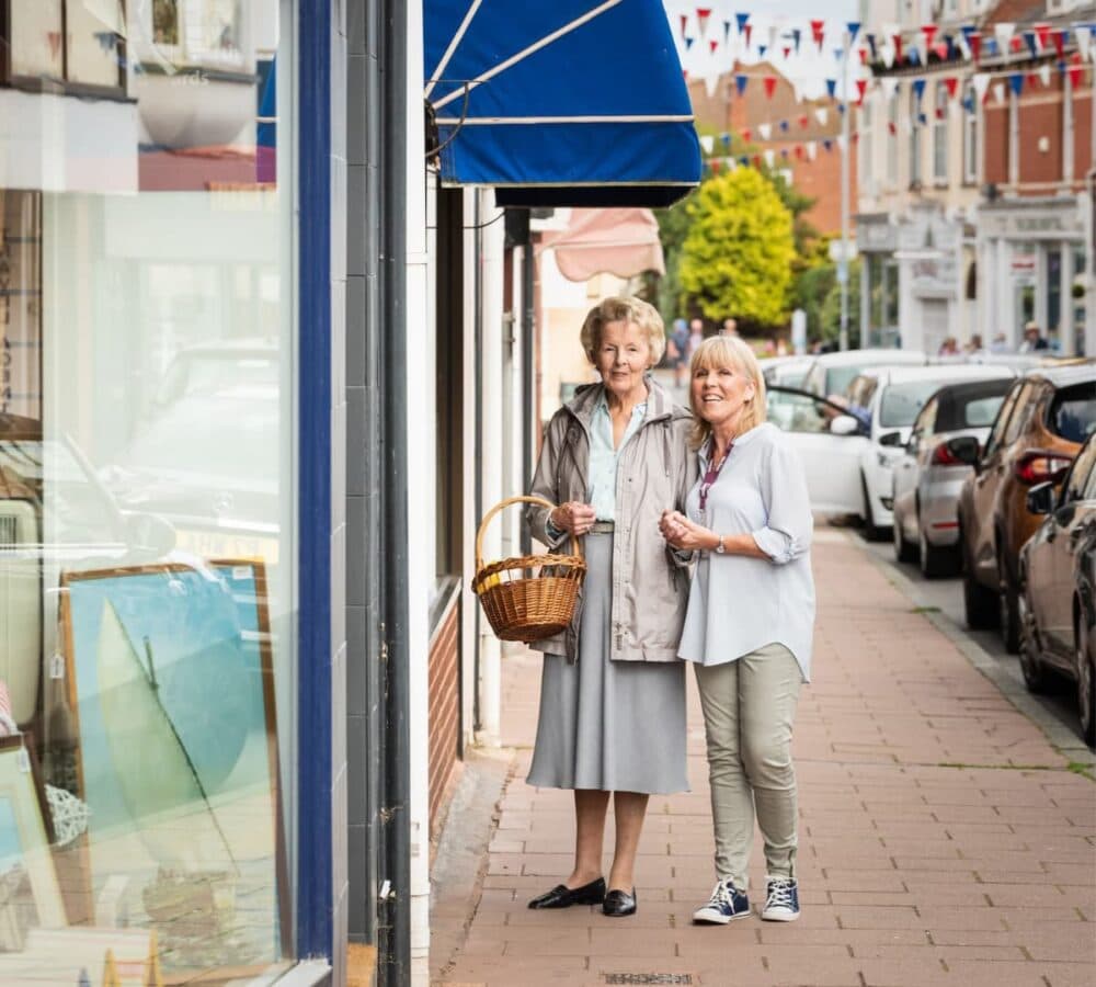 Senior outside the house with her carer and holding a brown basket