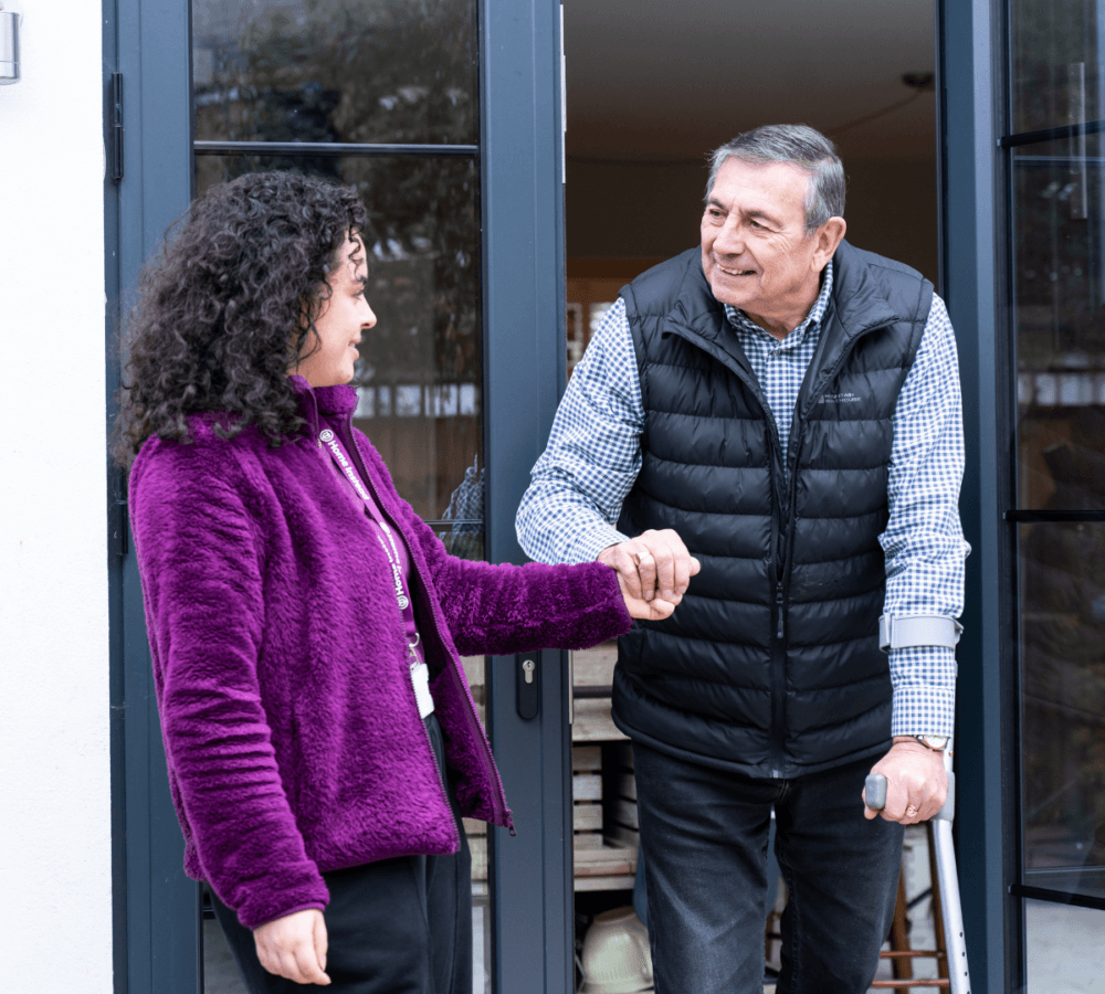 Senior man going out of the house with his carer helping her and both are smiling