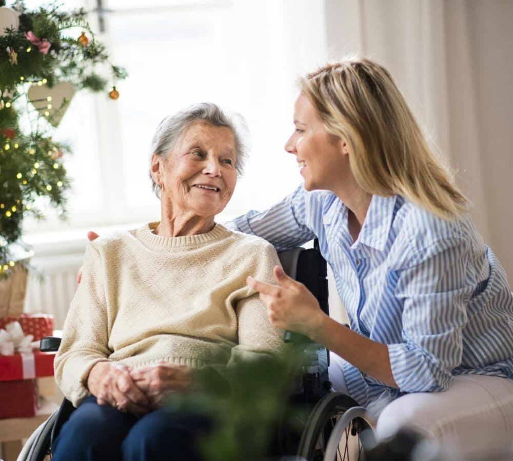 Senior woman on a wheelchair with her daughter looking at her both smiling and happy inside their home