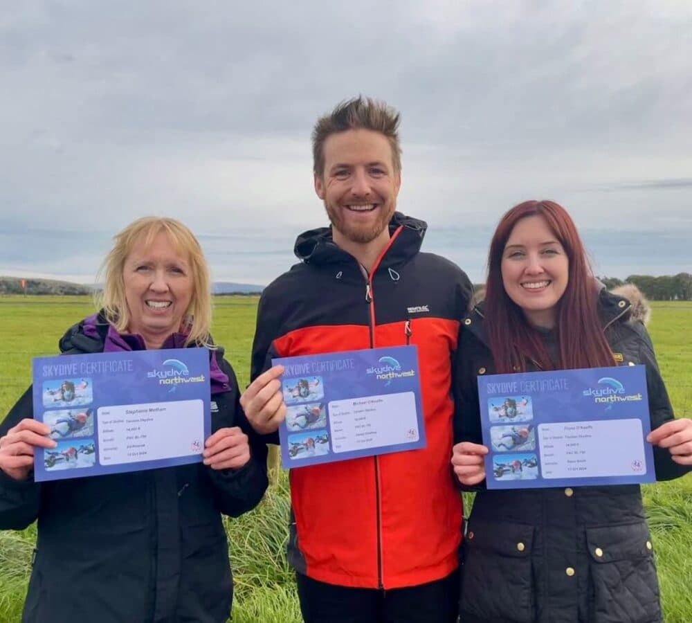 Three people on the fiels all happy and smiling while holding a certificate