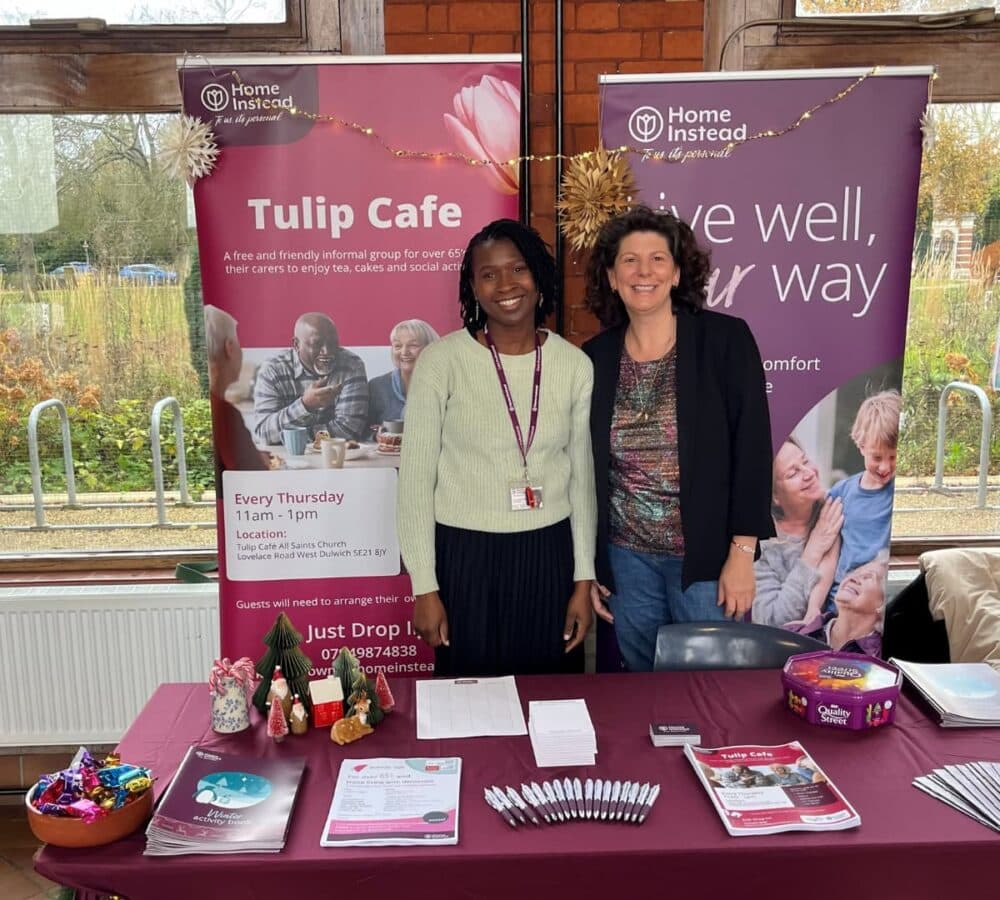 Two ladies both smiling while standing at Home Instead booth with purple banners at the back