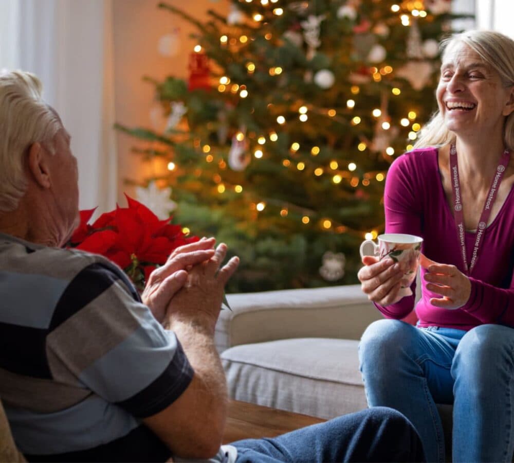 Woman laughing while talking to a senior man inside the home with a Christmas tree