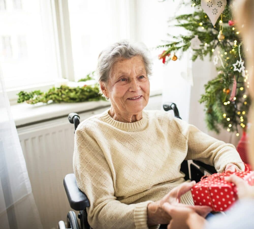 Senior woman receiving gift white sitting on a wheelchair inside her home