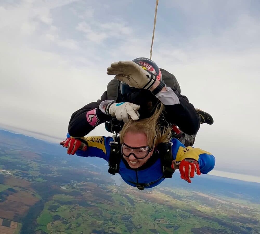 Woman skydiving together with a coach up in the air with a beautiful view of the sky