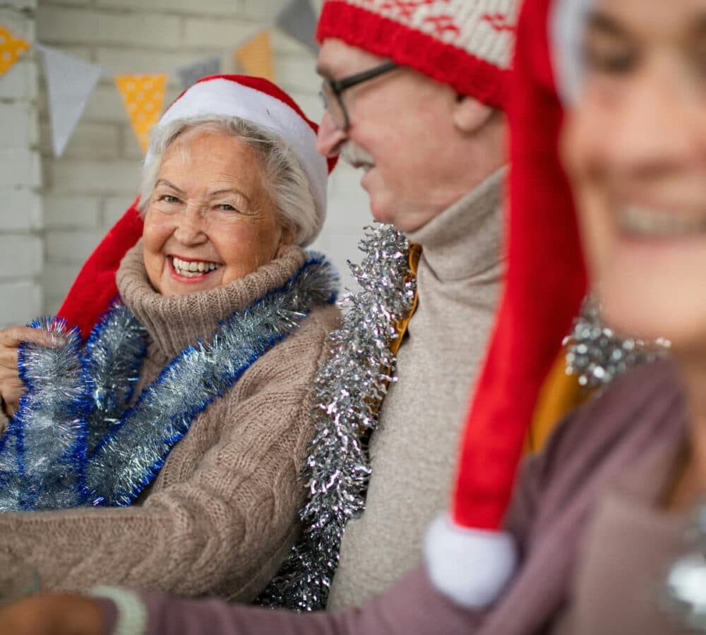 Senior woman wearing Santa hat smiling while sitting with other older adults