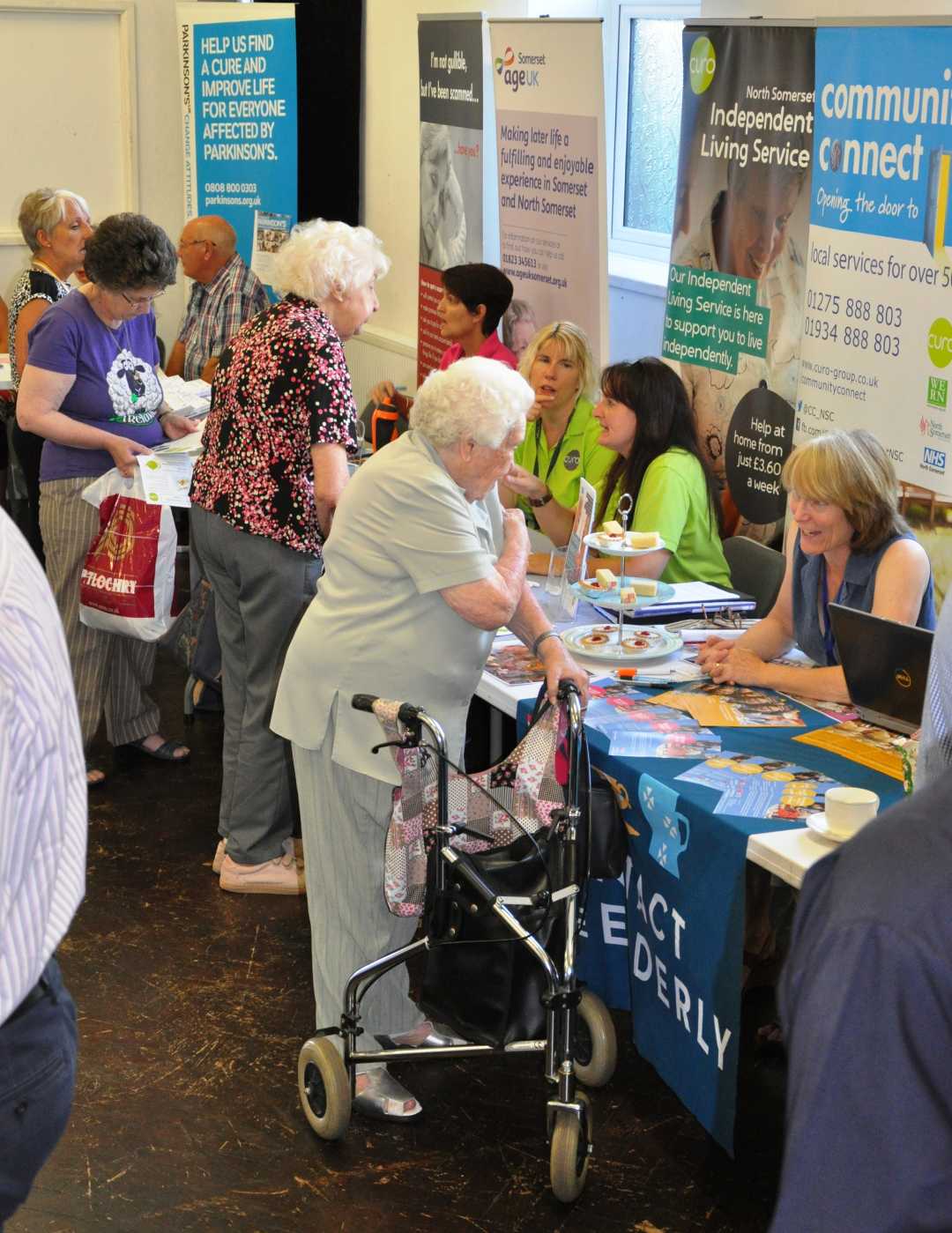 Elderly people talking to service providers at an information fair, with brochures on tables. - Home Instead