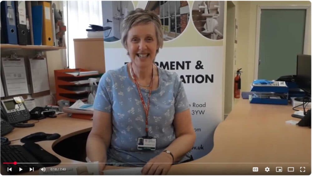 A woman sitting at a desk smiling. - Home Instead