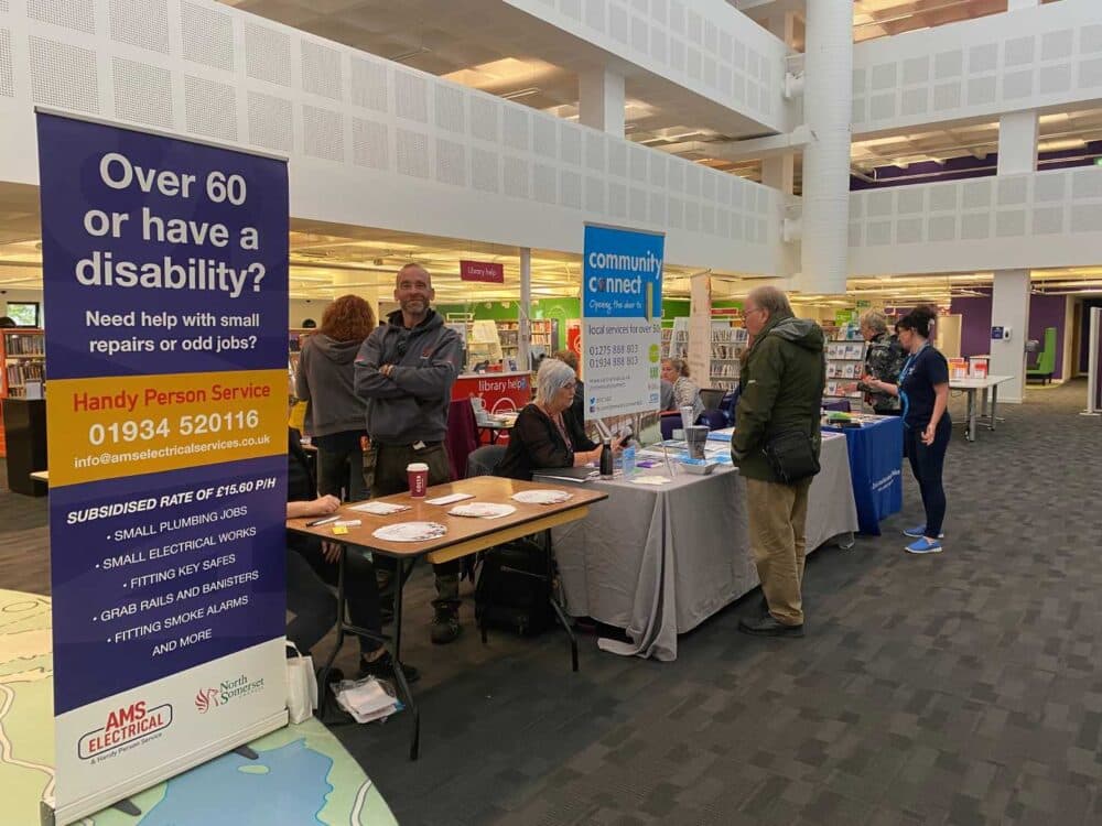 People at information tables in a library promoting community services for seniors and people with disabilities. - Home Instead