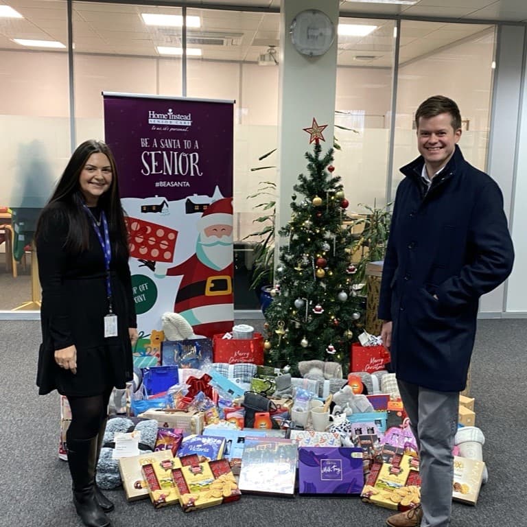 Two people standing in front of a Christmas tree and presents - Home Instead