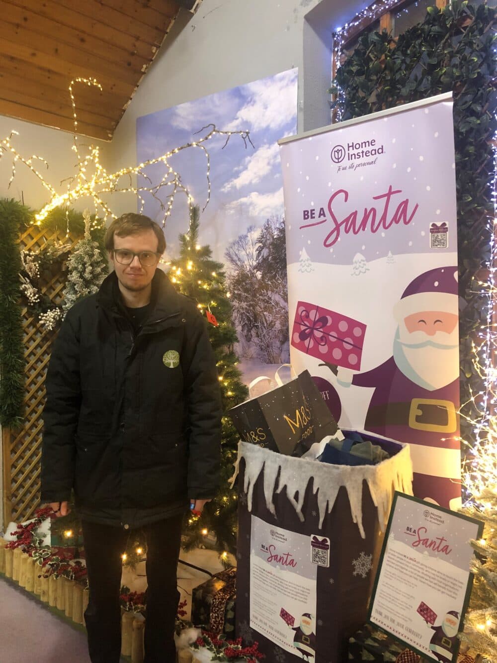 Man standing in front of Christmas display and gift collection point - Home Instead