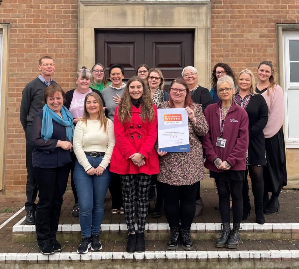 Group of people standing and smiling in front of a building while holding their 5 star employer award