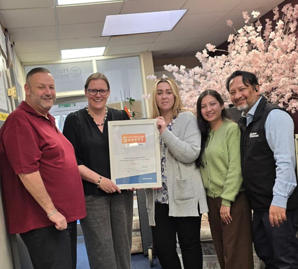 Group of people all smiling with a woman in the middle holding a plaque of award for a 5 star employer award