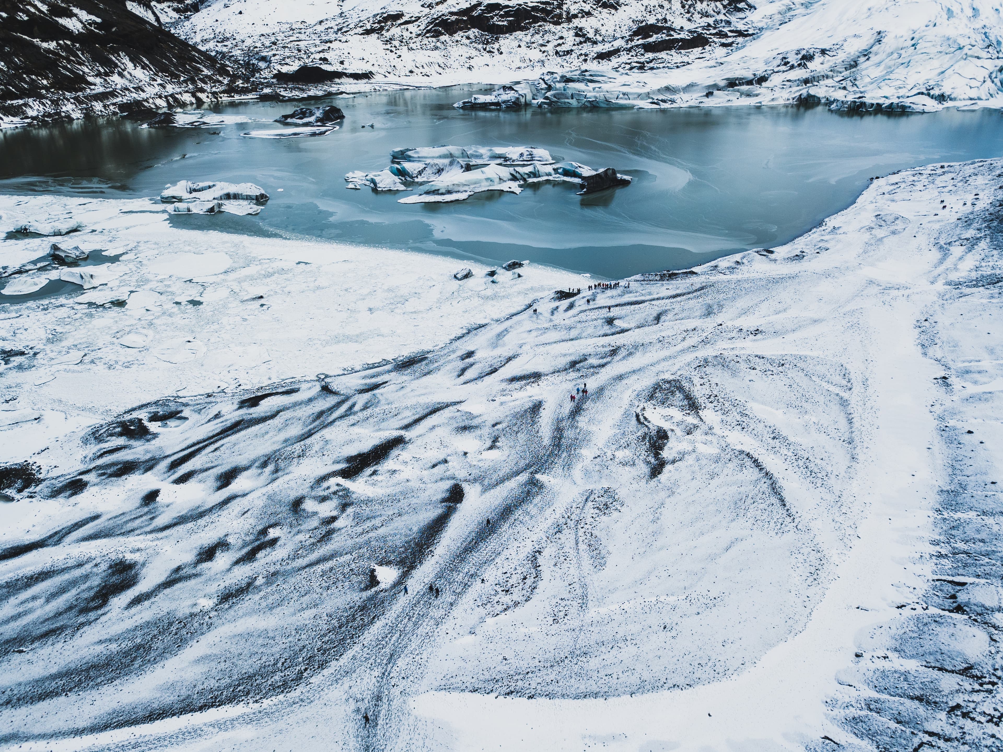 Aerial view of a snowy glacier with icy water and scattered icebergs under a cloudy sky. - Home Instead