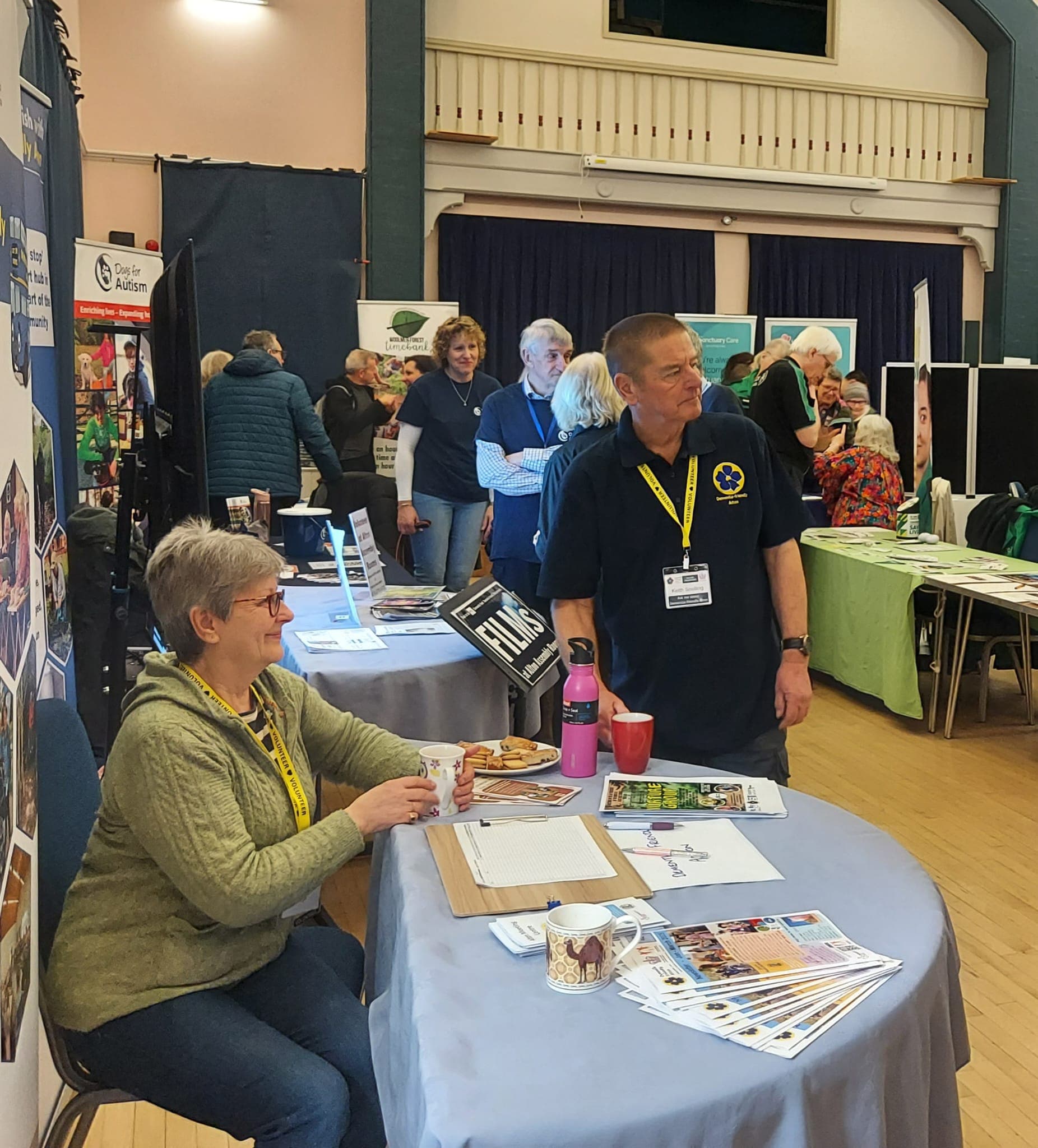 People at an indoor community event with tables, displays, and informational materials on display. - Home Instead