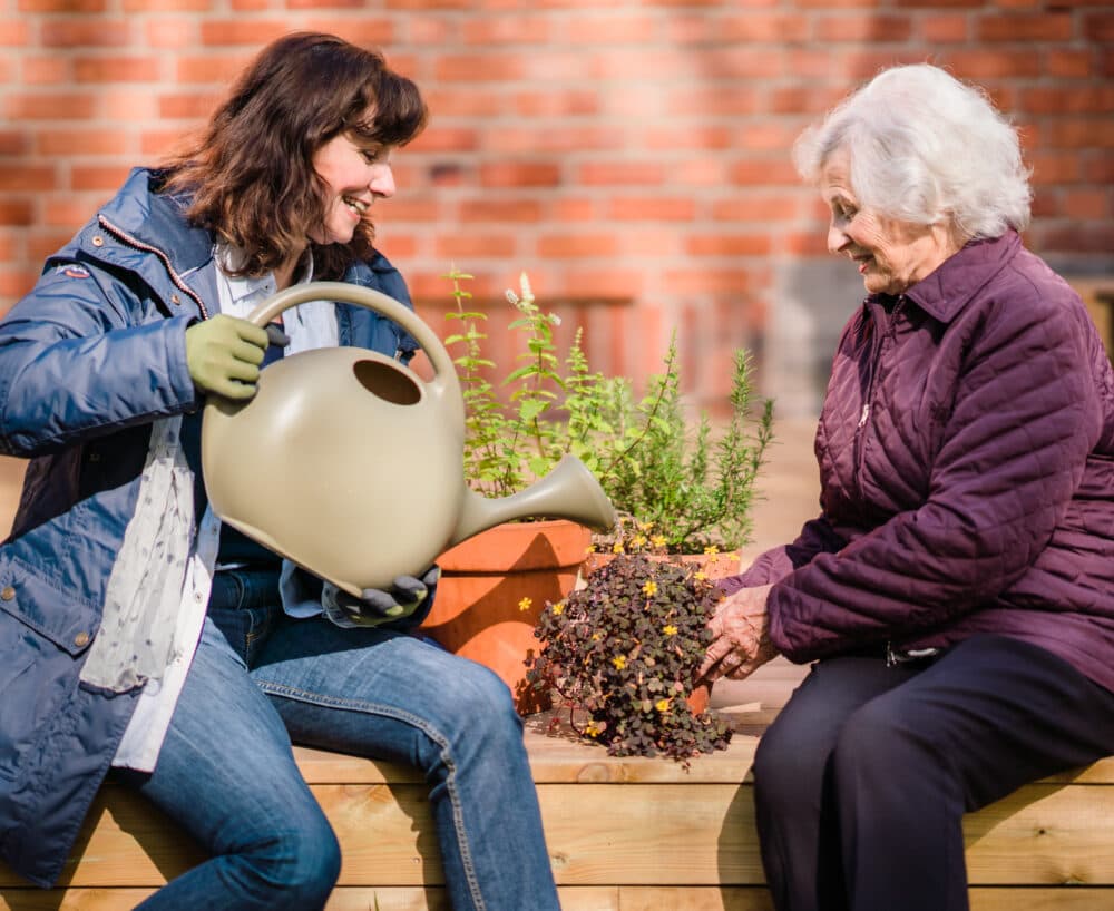 Home Instead live-in carer and her Home Instead live-in client watering plants in the garden