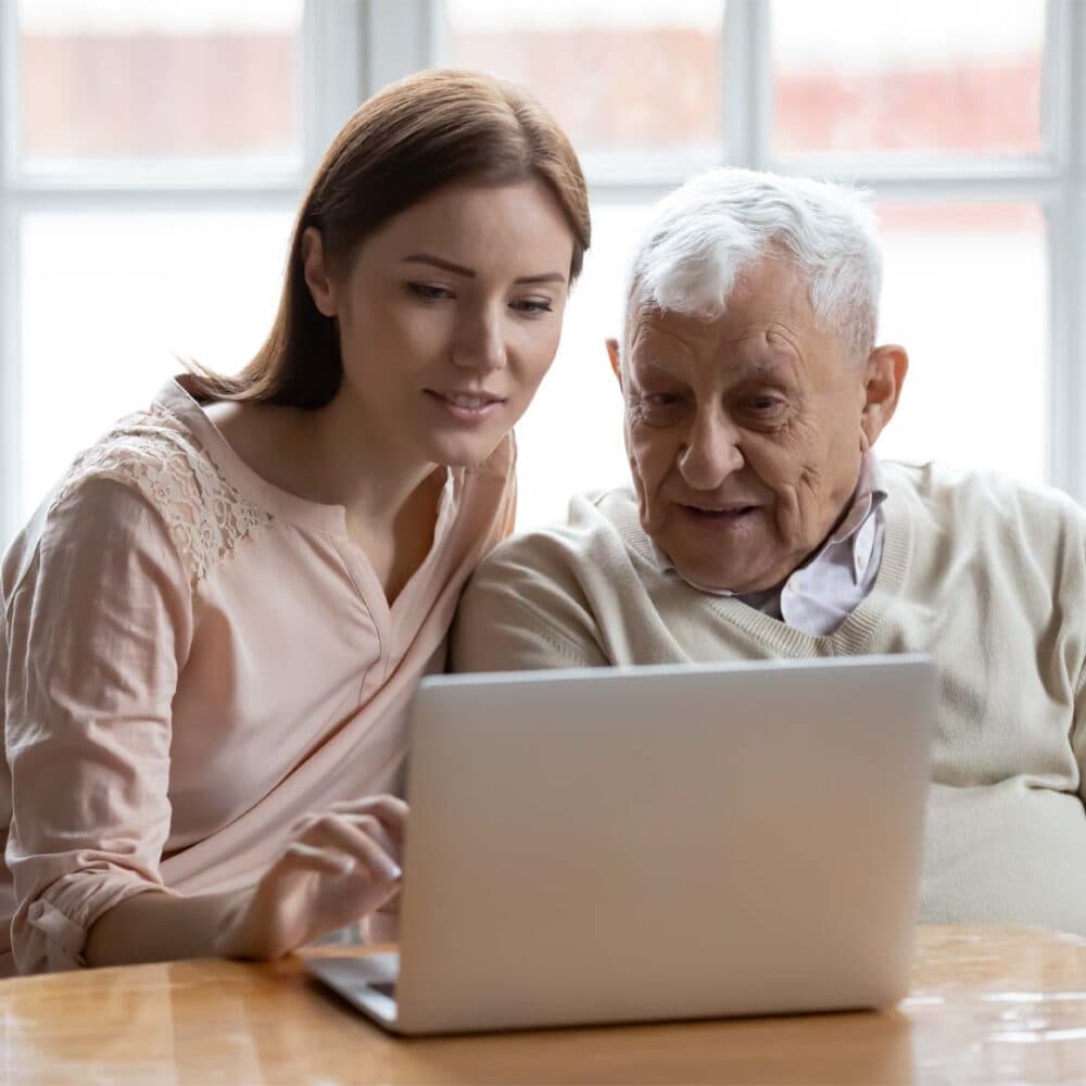 Daughter and elderly dad reviewing home care options on a laptap