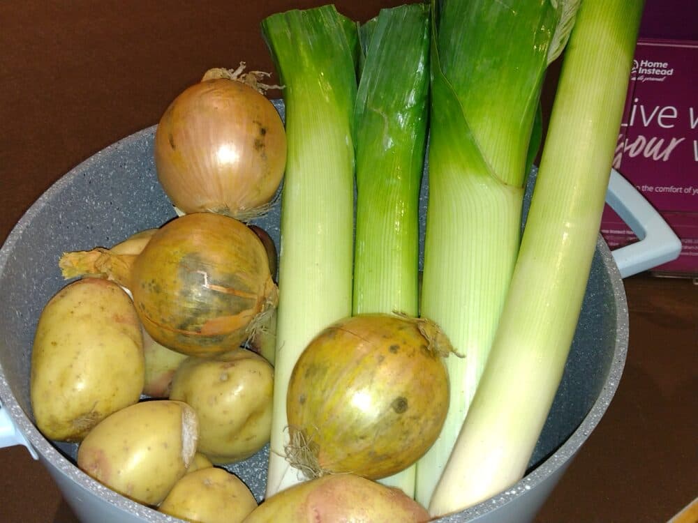 Potatoes, onions, and leeks in a gray cooking pot on a brown surface. - Home Instead