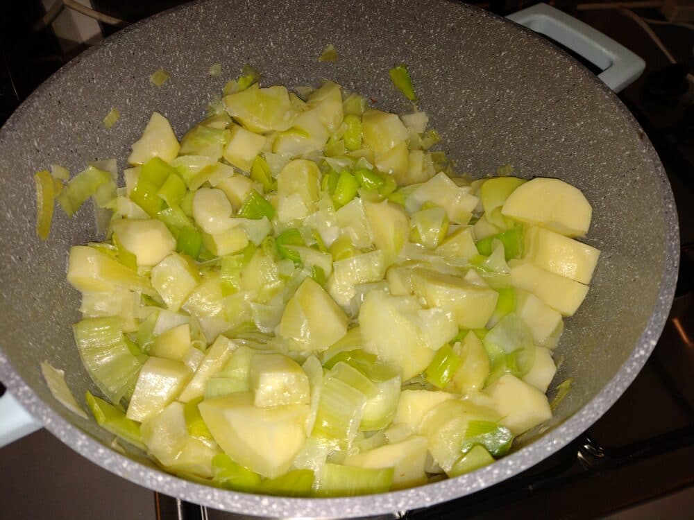 Chopped potatoes and leeks cooking in a large pot on a stovetop. - Home Instead