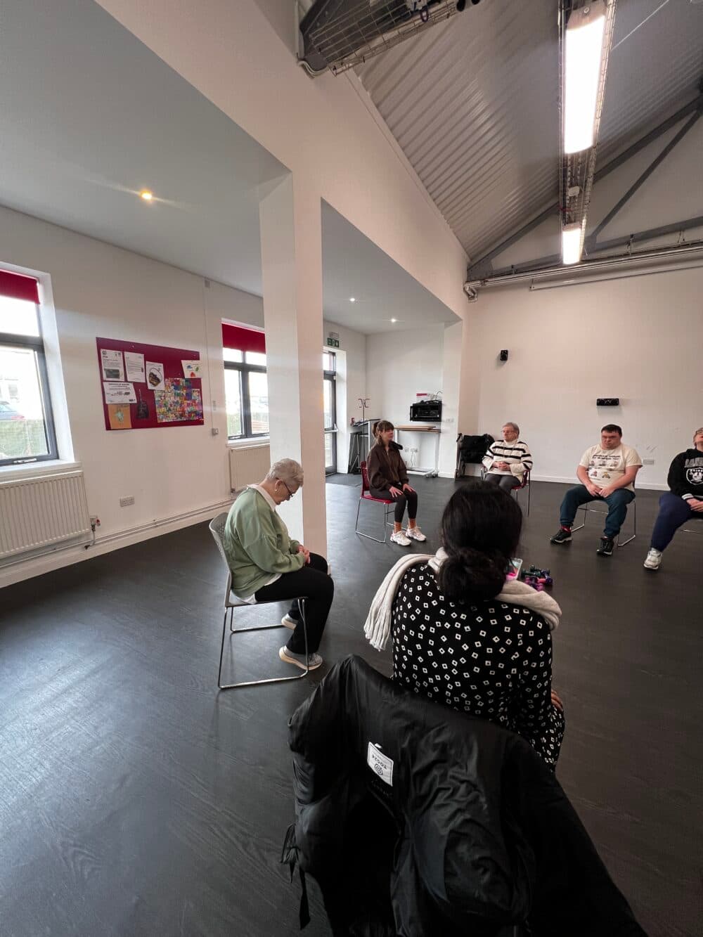 A small group of people sit in a circle in a bright room, participating in a group activity or discussion. - Home Instead