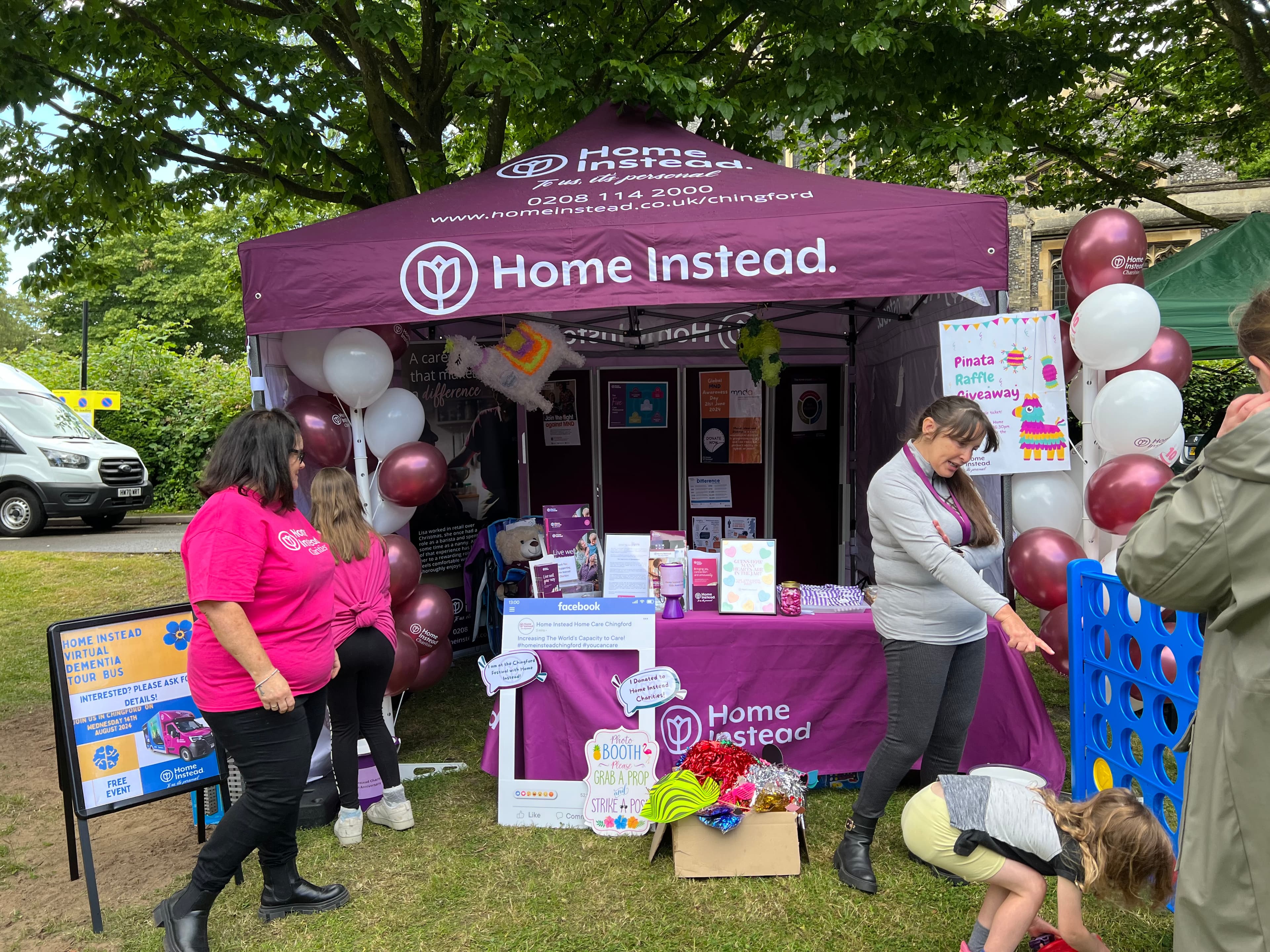 A Home Instead booth with balloons, games, and people interacting at a community event. - Home Instead