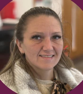 Woman with brown hair smiling, wearing a white coat and scarf, indoors with blurred background. - Home Instead