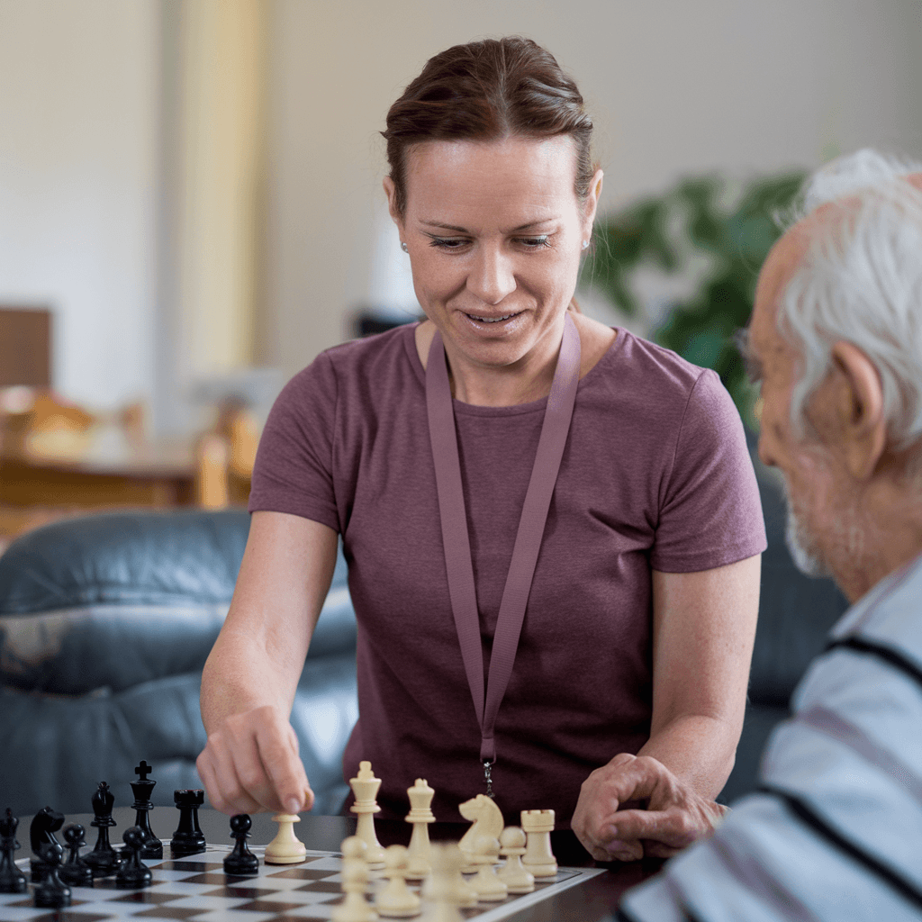 A woman and an elderly man are playing chess together at a table in a cozy room. - Home Instead