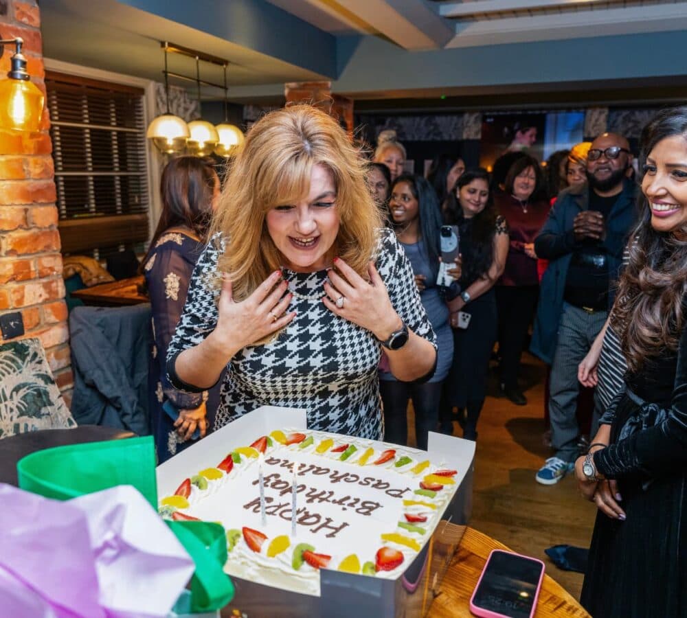 A woman happy and smiling with long blonde hair blowing a candle inside the restaurant with her friends