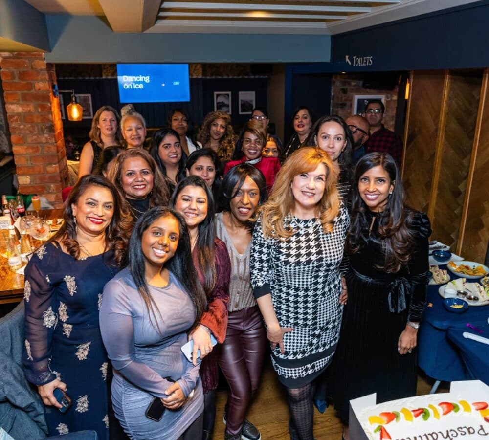 A group of smiling women posing together at a lively indoor party or celebration. - Home Instead